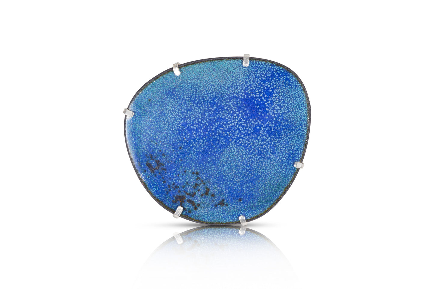 Handmade enamel brooch featuring a textured copper pebble shape with varying shades of blue enamel. The central area is dark blue, with lighter blue and black around the edges, inspired by the sea. The copper pebble is claw-set in recycled sterling silver, with a single brooch pin fastening.