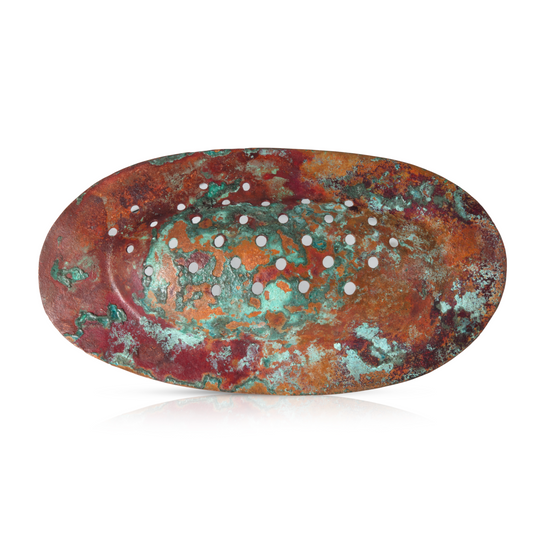 An oval brooch made from patinated copper in vibrant shades of rust red, orange, and turquoise green, featuring a textured surface with irregular patterns and small circular perforations evenly spaced across the design. The brooch has a sculptural, organic appearance, evoking a sense of natural erosion or weathering.

