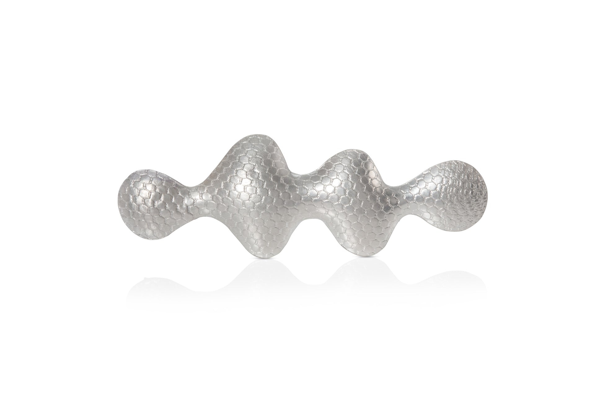 Wavy shaped silver brooch with a textured pattern on a white background.
