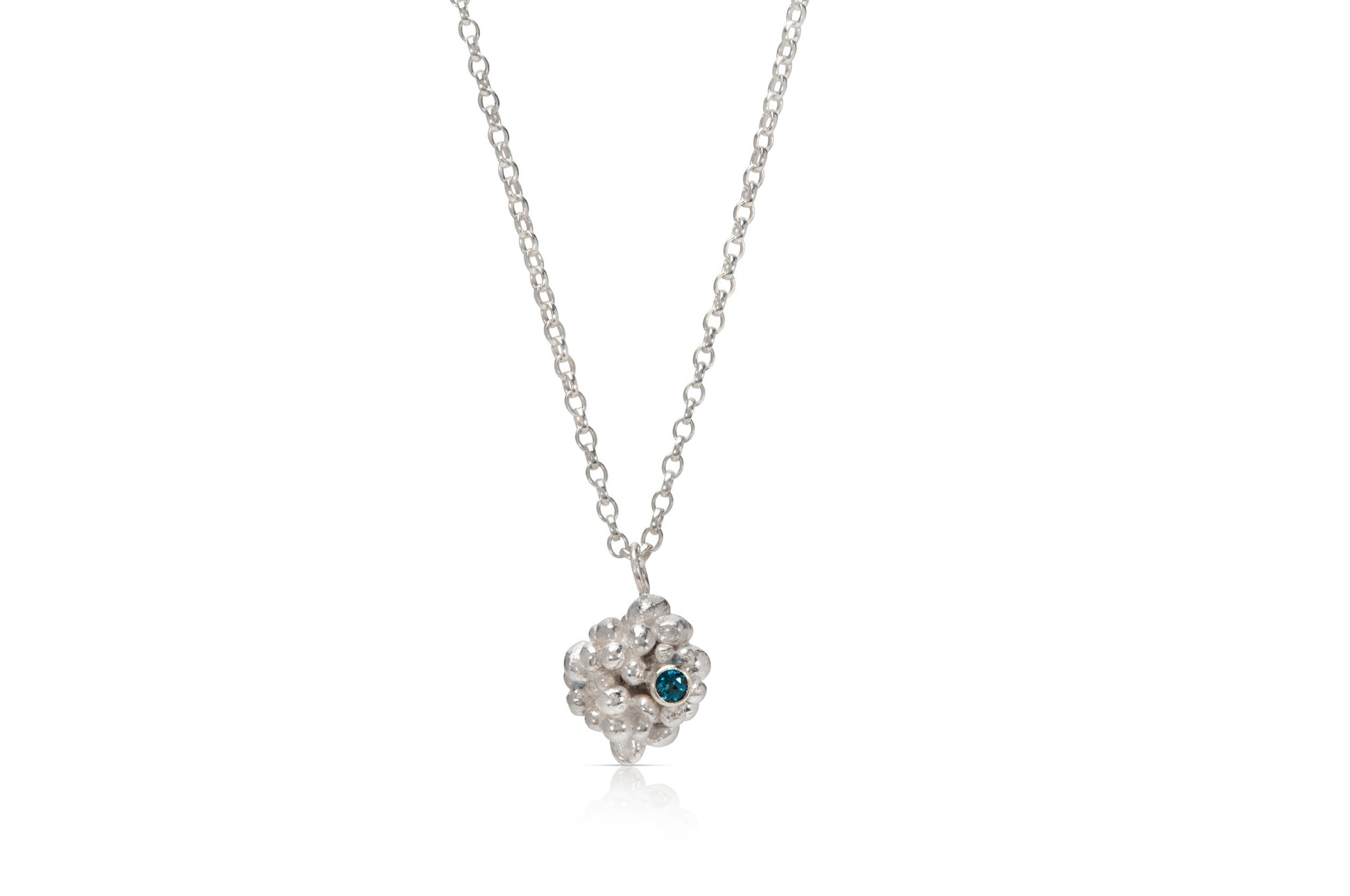 A silver raspberry shaped pendant made up of lots of small silver balls is on a white background. To the left on the pendant is a small, light blue stone.  The pendant hangs on a silver chain.