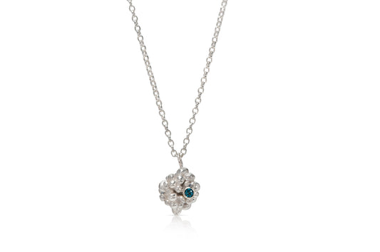 A silver raspberry shaped pendant made up of lots of small silver balls is on a white background. To the left on the pendant is a small, light blue stone.  The pendant hangs on a silver chain.